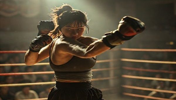 A high-definition image depicting a dynamic scene from a film set, featuring a strong female character, Rei, in an underground fighting ring. She is embodying both strength and tenderness, with a gritty yet emotional atmosphere surrounding her. The setting should evoke a sense of tension, with vivid details of the audience, fight choreography in motion, and visual hints of familial connections in the background, illustrating the duality of her identity as a mother and fighter. Soft lighting contrasts with the intensity of the fight, highlighting the feminist themes of ambition and empowerment.