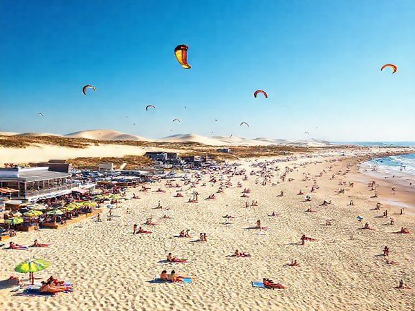 A breathtaking high-definition scene of Weststrand Sylt during a vibrant summer day, showcasing soft sandy beaches filled with sunbathers, colorful kites soaring overhead, and clear blue skies. In the background, capture the rolling dunes and stylish beachfront cafes bustling with visitors enjoying seafood and refreshing drinks. The atmosphere should exude warmth and joy, celebrating the lively summer spirit of this enchanting German island.