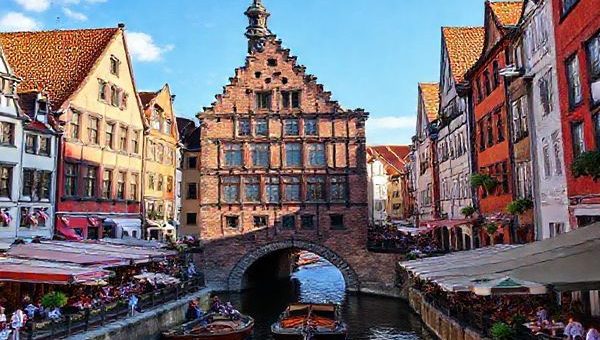 Create a high definition image of Lübeck Old Town in summer, showcasing its medieval architecture with vibrant colors and bustling market squares. Include the iconic Holsten Gate with sunlit canals, lively outdoor cafes, and people enjoying a boat tour along the Trave River. Capture the joyous atmosphere of the Lübeck Cultural Festival, with music and art blending into the charming cobbled streets lined with gabled houses under a clear blue sky.