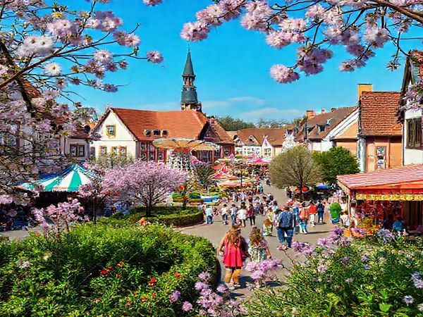 A captivating view of Recklinghausen in spring, showcasing vibrant blossoms and lush greenery, with families enjoying the Osterkirmes festival, amusement rides in the background, and cheerful pastel colors illuminating the streets. The scene captures the essence of renewal and outdoor joy, framed by picturesque historical architecture, all in high definition.