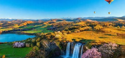 A vibrant scene showcasing the breathtaking landscapes of Waikato District in New Zealand, highlighting the rolling hills, lush pastures, and a majestic waterfall under a deep blue sky. Incorporate cultural elements such as a Maori cultural performance in the foreground and the Waikato Cherry Blossom Festival in full bloom nearby. Include various outdoor activities like kayaking on a serene lake and hot air balloons drifting in the sky during fall. Capture the essence of all four seasons, emphasizing the contrast of summer's warmth, winter's tranquility, autumn's vibrant colors, and spring's lively blossoms, all rendered in high definition.