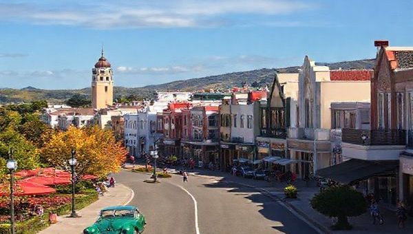 A breathtaking high-definition scene of Napier, New Zealand, showcasing its iconic Art Deco architecture surrounded by vibrant vineyards and lush landscapes. Capture the essence of each season: warm summer sunshine with bustling beachgoers, colorful autumn leaves along picturesque cycling trails, blooming spring gardens, and a serene winter backdrop with cozy cafes and quiet walks. Include elements like vintage cars during a festival, locals enjoying wine tastings, and panoramic views of Hawke's Bay to embody the rich cultural tapestry of this coastal city.