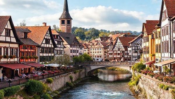 Create a high-definition image of Heilbronn in each season: vibrant summer filled with festivals and lush vineyards, cozy winter with frosty streets and a Christmas market, colorful autumn showcasing vineyards in hues of red and gold, and a blossoming spring with blooming flowers and lively outdoor activities. Include charming architecture and the Neckar River flowing through the scenes to capture the town's essence.