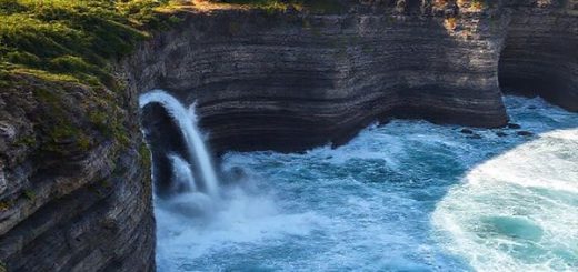 A breathtaking view of Punakaiki Pancake Rocks on the rugged west coast of New Zealand's South Island, showcasing the unique limestone formations resembling stacked pancakes. Capture the powerful surf crashing through blowholes, creating dramatic water spouts against the backdrop of the mesmerizing Tasman Sea. The lush rainforest surrounding the rocks should be vibrant, reflecting the enchanting beauty and tranquility of different seasons like summer's bright green foliage and winter’s clear skies. High-definition, emphasizing the dynamic interaction of land and sea in a serene yet captivating atmosphere.