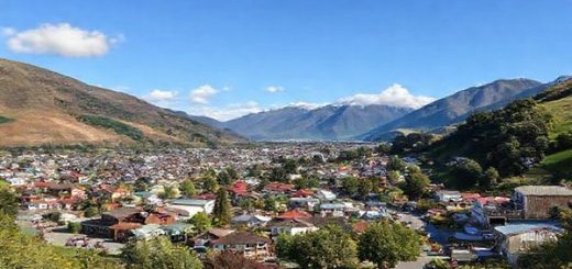 A scenic view of Paeroa, New Zealand, showcasing the charming small town nestled in the picturesque Karangahake Gorge. Capture the vibrant atmosphere of summer with clear blue skies, lush greenery, and tourists enjoying local festivals. Include iconic elements like the Lemon & Paeroa drink, historic mining tunnels, and colorful flower displays in spring. Set the scene in high definition, highlighting the unique blend of culture and natural beauty across different seasons.