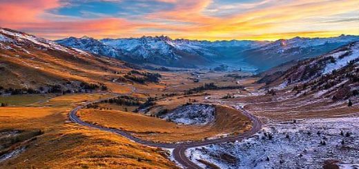 **A stunning high-definition view of Lindis Pass, showcasing the dramatic contrast of all four seasons in one image: vibrant golden fields and lush greenery in summer, a serene snowy landscape in winter, a tapestry of autumn hues with shades of gold, orange, and red in fall, and blooming wildflowers with clear blue skies in spring. The winding roads should be visible, inviting travelers into this breathtaking alpine paradise, with mountains in the background and a surreal sunset illuminating the scene.**