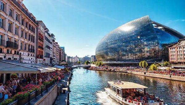 A stunning high definition image of HafenCity in summer, showcasing the vibrant atmosphere with outdoor festivals, bustling streets, and the striking Elbphilharmonie in glass reflected in the sun. Include people enjoying the waterfront cafes, blooming flowers, and a lively boat tour on the Elbe River, all under a clear blue sky.