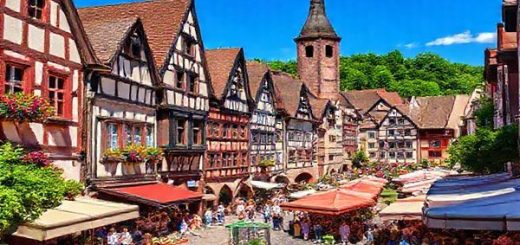 "Create a high definition image of Freiburg, Germany in the heart of summer, showcasing cobbled streets bustling with locals and tourists, vibrant markets filled with colorful stalls, and lush greenery surrounding the city. The scene should capture the warmth of the sun, the atmosphere of lively festivals, and the picturesque architecture of the medieval old town, all under a clear blue sky."