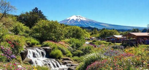 Create a high-definition image of Stratford District in New Zealand during spring, showcasing a vibrant landscape filled with blooming wildflowers, lush green foliage, and waterfalls flowing abundantly. Include the iconic Mount Taranaki in the background under a bright blue sky. Feature local festivals with stalls offering fresh produce and artisans displaying crafts, capturing the lively atmosphere of community engagement. Bright, soft sunlight enhances the colors, evoking a sense of rejuvenation and vitality in this picturesque setting.