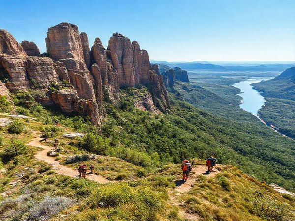 A breathtaking high-definition landscape of the Elbe Sandstone Mountains, showcasing the dramatic rock formations adorned with vibrant summer greenery and the glistening Elbe River in the background. Include hikers on the trails enjoying the outdoor adventure, with a clear blue sky overhead.