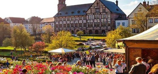 A picturesque view of Osnabrück in late spring, showcasing blooming flowers in vibrant colors across lush parks, with the historic Town Hall of the Peace of Westphalia standing majestically in the background. People are enjoying a lively Stadtfest, with stalls displaying local crafts and delicious foods, while cheerful street performers entertain in the foreground. The sun casts a warm glow, creating an inviting atmosphere filled with laughter and joy. Please create this image in high definition.