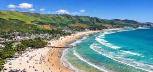 A high-definition image showcasing the stunning landscapes of Manukau District in New Zealand during summer. Capture the vibrant beaches like Maraetai and Weymouth with sunbathers and water sports, surrounded by lush greenery and rolling hills of the Hunua Ranges. Include the bustling atmosphere of a cultural festival, with colorful stalls and local Maori performances, all under a bright blue sky. The scene should convey the dynamic energy of summer while highlighting the seamless blend of nature and urban life.