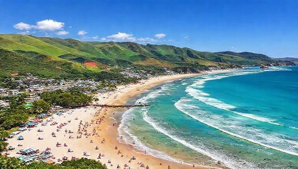 A high-definition image showcasing the stunning landscapes of Manukau District in New Zealand during summer. Capture the vibrant beaches like Maraetai and Weymouth with sunbathers and water sports, surrounded by lush greenery and rolling hills of the Hunua Ranges. Include the bustling atmosphere of a cultural festival, with colorful stalls and local Maori performances, all under a bright blue sky. The scene should convey the dynamic energy of summer while highlighting the seamless blend of nature and urban life.