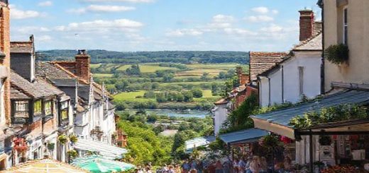 A picturesque scene of Feilding in summer, showcasing a charming street lined with Edwardian architecture, vibrant local market stalls brimming with fresh produce, and lush green parks. Families are enjoying picnics and leisure activities under a bright, sunny sky, while a backdrop of tranquil rivers and distant vineyards adds to the idyllic atmosphere. The image should capture the essence of community and nature in high definition.