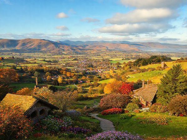 A panoramic view of the Matamata-Piako District in all four seasons, showcasing summer's vibrant festivities at Hobbiton, autumn's rich golden foliage, winter's misty hills, and spring's blooming flowers, all harmoniously blended into a single high-definition landscape. Add a touch of whimsical charm to reflect its connection to Middle-Earth.