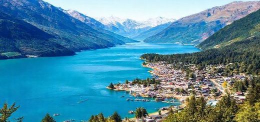 A breathtaking high-definition landscape of Queenstown-Lakes District in summer, showcasing the vibrant blue waters of Lake Wakatipu surrounded by rugged mountains and lush green forests. Include adventure seekers kayaking and paddleboarding on the lake. The town of Queenstown buzzes with energy, featuring outdoor festivals and colorful market stalls under a clear, sunny sky. Capture the essence of summer vibrancy and natural beauty in this paradise setting.