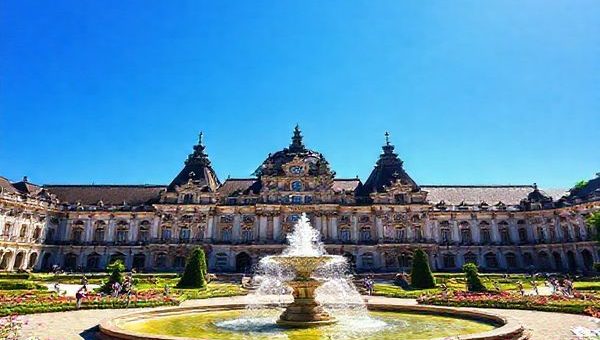 A stunning high-definition image of Zwinger Palace in Dresden, Germany, showcasing its magnificent Baroque architecture surrounded by lush summer gardens in full bloom. Sunlight sparkles on the Fountain Court, with visitors enjoying peaceful strolls among vibrant flowers and greenery. Capture the exquisite details of the palace’s ornate facades under a bright blue sky, while the atmosphere exudes a sense of cultural richness and serenity.