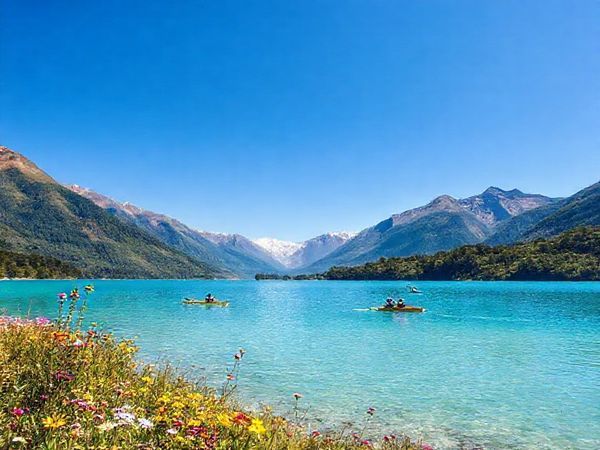A breathtaking high-definition landscape of Lake Clearwater, New Zealand, showcasing the serenity of summer with vibrant azure waters and surrounding lush greenery, framed by majestic mountains under a clear blue sky. Include water sports enthusiasts kayaking and windsurfing, alongside blooming wildflowers and active wildlife like black stilts. The scene should evoke a sense of adventure and tranquility, capturing the essence of this hidden gem in Canterbury.
