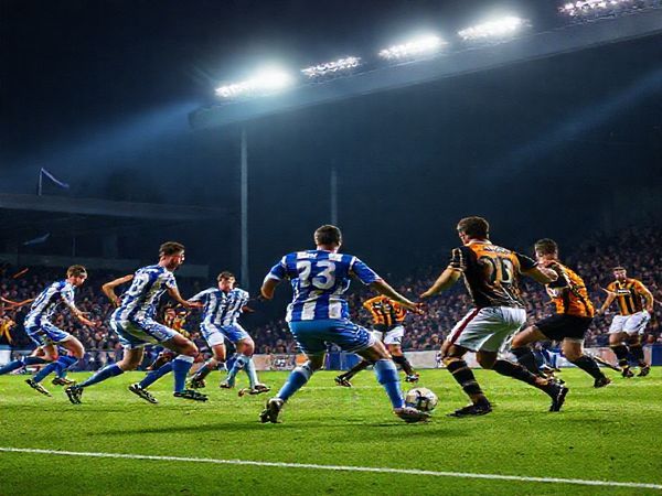 A dramatic high-definition scene depicting a fierce football match at Edgeley Park, where Stockport County and Cambridge United clash under floodlights. Stockport's energetic players press intensely, wearing blue and white, while Cambridge's tactical maestros, in amber and black, orchestrate their play with determined composure. The crowd is electrified, with flags waving and tension palpable in the air. Capture the dynamic contrasts between Stockport's high-octane style and Cambridge's disciplined tactics, with a backdrop of vibrant football action, soaring emotions, and a hint of an unexpected twist in the eager anticipation of the FA Cup.