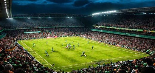 High definition image of a dramatic football match scene depicting Plymouth Argyle and Bradford City in a tense League One clash. The stadium is electric with crowds wearing green and gold cheering passionately. Show Plymouth's players, showcasing their tactical prowess and strong defense, contrasted with Bradford's gritty attackers making a swift counter-attack. Capture the intensity and emotion of the game, with a darkening sky and stadium lights illuminating the pitch.