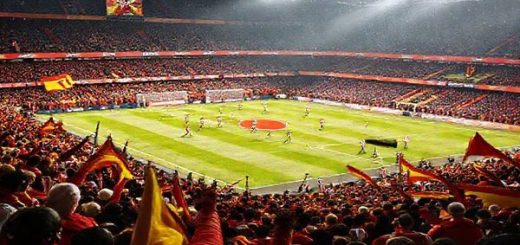A dramatic football match scene between Rayo Vallecano and Valencia in a packed stadium under December's chill, with fans waving flags and banners in vibrant red and yellow. Rayo Vallecano players, known for their tenacity, pressing aggressively to win the ball, while Valencia's youthful stars display a mix of controlled aggression and creativity on the pitch. The atmosphere is electric, capturing the essence of rivalry, momentum, and the beautiful game. Make the image in high definition.