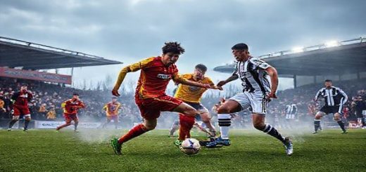 A dramatic football pitch under a winter sky, showcasing a fierce battle between the Stenhousemuir Warriors, wearing their vibrant red and yellow kits, and the slick, strategic Hamilton Academical in their classic black and white attire. In the foreground, players engage in a tense midfield tussle, with the ball swirling amidst a crowd of passionate fans, banners waving, and mist rising from the cold ground. Capture the intensity of the moment with dynamic poses and expressions reflecting determination and strategy. Make the image in high definition.