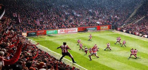 A high-definition image depicting a tense moment during the League Two match between Swindon Town and Cheltenham Town in December 2025. Capture a crowded, vibrant stadium filled with passionate fans waving team colors, as players from both teams engage in a fierce midfield battle, showcasing Swindon’s tenacious defense against Cheltenham’s strategic offense. The atmosphere is electric, with snow gently falling, and festive decorations subtly incorporated, symbolizing the height of the football season.