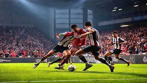High definition image of a dramatic football match between Grimsby Town and Wealdstone, featuring players in vibrant kit colors fiercely contesting the ball in a packed stadium under bright lights. Capture the tension of the midfield battle, showcasing Grimsby’s disciplined defense and Wealdstone’s dynamic play, with passionate fans in the stands adding to the atmosphere. The scene should evoke excitement and anticipation, reflecting the spirit of the FA Cup in December 2025.