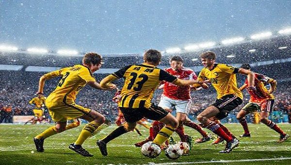 "An intense football match scene under a snowy sky, featuring a dynamic clash between the Young Boys and Lille. The Young Boys, in bright yellow and black jerseys, exhibit high energy and a fast-paced game, while Lille players in red and white uniforms display tactical precision and defensive solidity. The stadium is packed with enthusiastic fans amidst flurries of snow, and the floodlights illuminate the fierce competition. Capture the emotions of determination, excitement, and rivalry in high definition."