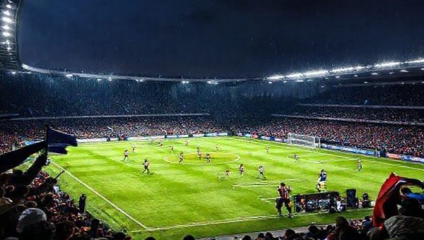 A dramatic football showdown under the floodlights on a chilly December evening in 2025, capturing the intense clash between Auxerre and Metz. The scene features passionate fans waving flags, a tense midfield battle with players in motion, and a vibrant soccer pitch illuminated with bright stadium lights. Capture the contrasting styles: Auxerre's solid, defensive formation on one side and Metz's dynamic, fluid attacking play on the other. High definition, showcasing the detailed expressions and movements of the players and the excitement in the stands.