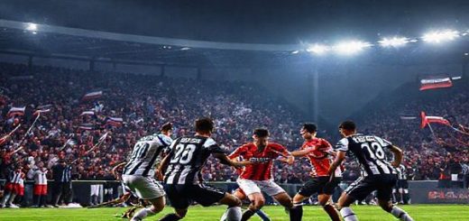 A high-definition image of a dramatic football match between Nice and Angers under the floodlights, showcasing the fierce intensity on the pitch. The scene captures the vibrant colors of the teams' jerseys as players clash in a tactical battle, with Nice's attackers poised to break through Angers' disciplined defense. In the background, an enthusiastic crowd waves flags in a crisp December night, emphasizing the excitement and anticipation of the clash. The atmosphere should be electric, with a blend of joy, tension, and passion for the beautiful game.