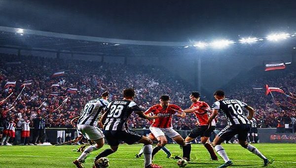 A high-definition image of a dramatic football match between Nice and Angers under the floodlights, showcasing the fierce intensity on the pitch. The scene captures the vibrant colors of the teams' jerseys as players clash in a tactical battle, with Nice's attackers poised to break through Angers' disciplined defense. In the background, an enthusiastic crowd waves flags in a crisp December night, emphasizing the excitement and anticipation of the clash. The atmosphere should be electric, with a blend of joy, tension, and passion for the beautiful game.