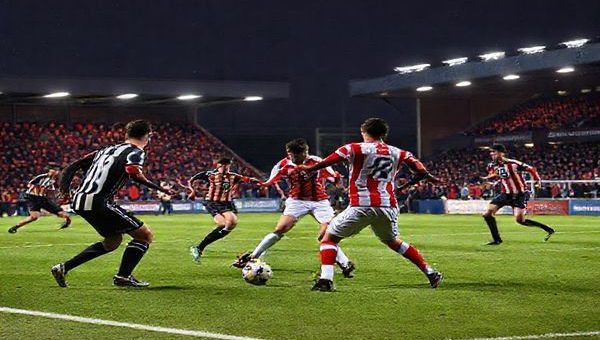 A high-definition image of a tense and dramatic soccer match between Doncaster Rovers and Stockport County on a brisk December evening. The scene captures players in action, showcasing Doncaster's resilient style with a solid defensive line and Stockport's counter-attacking agility. The vibrant stadium is alive with passionate fans, illuminated by floodlights, as the players clash on the field, highlighting the intense tactical battle and emotions of this League One encounter.