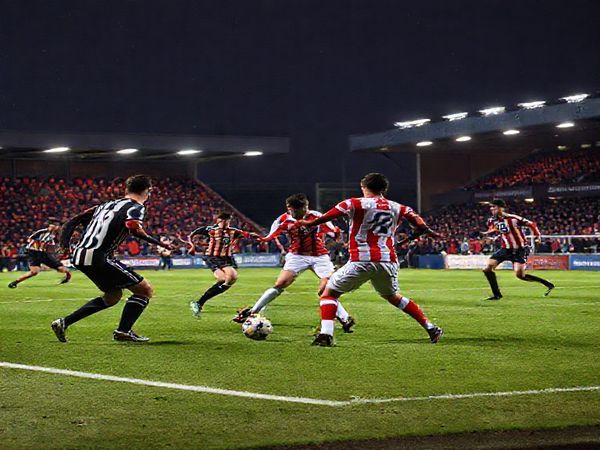 A high-definition image of a tense and dramatic soccer match between Doncaster Rovers and Stockport County on a brisk December evening. The scene captures players in action, showcasing Doncaster's resilient style with a solid defensive line and Stockport's counter-attacking agility. The vibrant stadium is alive with passionate fans, illuminated by floodlights, as the players clash on the field, highlighting the intense tactical battle and emotions of this League One encounter.