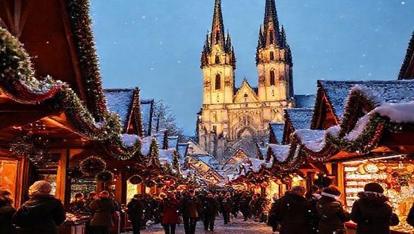Create a high definition image of the Christkindlesmarkt in Nuremberg during winter, with over 180 charming wooden stalls adorned in red and white cloth, surrounded by twinkling lights and glistening snow. Capture visitors sipping warm mulled wine and enjoying festive treats like toasted almonds and gingerbread, with a backdrop of the majestic Frauenkirche illuminated in the evening glow, while carolers fill the air with Christmas melodies.
