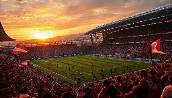 A vibrant football scene depicting a high-stakes match between FC Drita and AZ Alkmaar, filled with intense emotion. The stadium, packed with passionate fans waving flags, showcases Drita's "Warriors of Gjilan" in their striking kit, preparing for a counter-attack, while AZ’s players exhibit their intricate passing and attacking flair. The backdrop features a dramatic sunset over Gjilan, highlighting the tension and aspirations of both teams. Render this image in high definition.