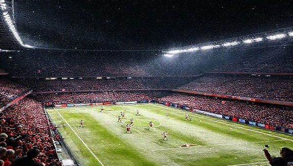 A dramatic night scene of a packed stadium under bright floodlights, showcasing a fiercely contested football match between Freiburg and Red Bull Salzburg. The players are in action, illustrating Freiburg's disciplined formation against Salzburg's aggressive pressing style. Snow lightly falls on the field, adding to the winter atmosphere. Tension and ambition are palpable in the air as fans cheer passionately in vibrant team colors. High definition, with a focus on dynamic movement and intense expressions.