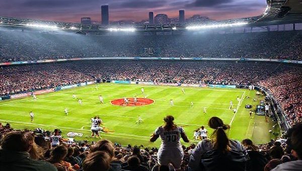 A high definition image capturing the intense atmosphere of a women's football match between Real Madrid Women and Wolfsburg Women at the Alfredo Di Stéfano Stadium. The scene shows vibrant fans in the stands, colorful team jerseys clashing on the field, and dynamic action as players like Claudia Zornoza and Alexandra Popp engage in a tactical battle. Dramatic lighting enhances the urgency and excitement of this Women's Champions League showdown on December 9, 2025, with a backdrop of the iconic Madrid skyline.