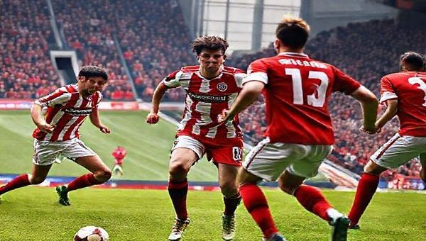 High-definition image prompt: A dramatic scene of a tense football match, featuring Lincoln City in their traditional red and white kit and Barnsley in their iconic red jersey. The players are locked in an intense duel on a vibrant green pitch, with a packed stadium filled with passionate fans chanting. The atmosphere is electric, highlighting the contrasting styles of Lincoln's gritty defense and Barnsley's fluid attacking play. A determined forward makes a decisive run towards the goal, while a midfielder prepares to launch a counter-attack. Capture the emotion, excitement, and tactical intensity of this League One clash in stunning detail.