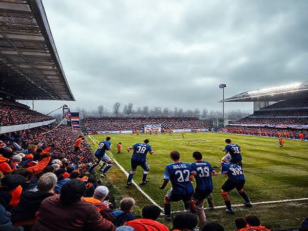 A dramatic football scene set in the Doonhamers' home ground under a crisp December sky, showcasing Queen of the South FC in navy blue jerseys, forming a disciplined defensive line, contrasted against the vibrant, energetic Cove Rangers in bright orange, launching a fast-paced attack. The stadium is packed with passionate fans, flags waving, as anticipation fills the air. Include dynamic movements, a classic football atmosphere, and the intensity of the clash, all in high definition.