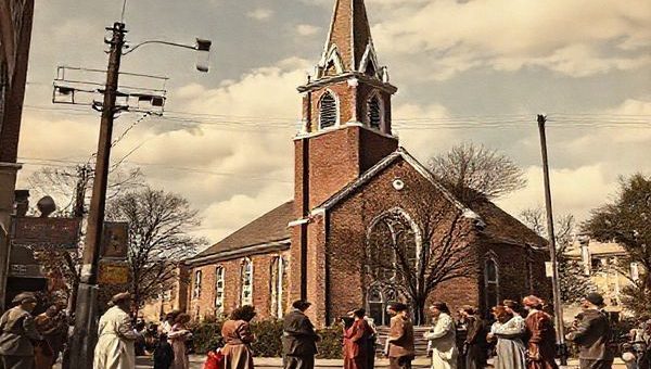 "High-definition image of a 1940s street scene featuring a church with a tall steeple, set against a backdrop of post-war optimism and uncertainty. Capture a diverse group of people engaging in conversation outside the church, reflecting hope and curiosity about the future of religion. Incorporate elements of early technology, like radio antennas and film posters of clergy in movies, to symbolize the church's evolving role in a changing world."