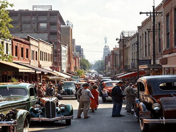 A vibrant 1930s street scene, showcasing the blend of hope and anxiety during the Great Depression. Imagine bustling urban life with people engaging in lively conversation, surrounded by early automobiles, a mix of modest and futuristic architecture, and innovative farming equipment in the background. Capture the contrasts between rural and urban community life, with lush greenery and a subtle whisper of technology, all in high definition.