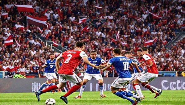 High-definition image of a tense football match between Czechia and Gibraltar, showcasing Czech players in red and white uniforms executing a strategic play on the field, with the blue and white-clad Gibraltar team defending fiercely. The setting is a vibrant stadium filled with passionate fans waving flags and banners, capturing the emotional intensity of this World Cup Qualifier clash. The foreground focuses on the dynamic movement of players, while the background shows a packed audience, creating an atmosphere of rivalry and excitement.