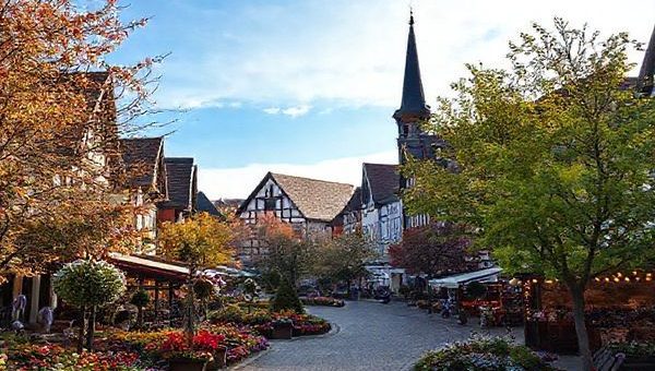 **Create a high-definition image of Gütersloh, Germany, showcasing the enchanting charm of each season: vibrant summer parks filled with blooming flowers and outdoor concerts, a cozy winter Christmas market sparkling with fairy lights, colorful autumn leaves in serene landscapes, and colorful spring flowers beneath a bright blue sky. Include elements like family picnics, local festivals, and cultural events, all blending harmoniously into a picturesque representation of this hidden gem in North Rhine-Westphalia.**