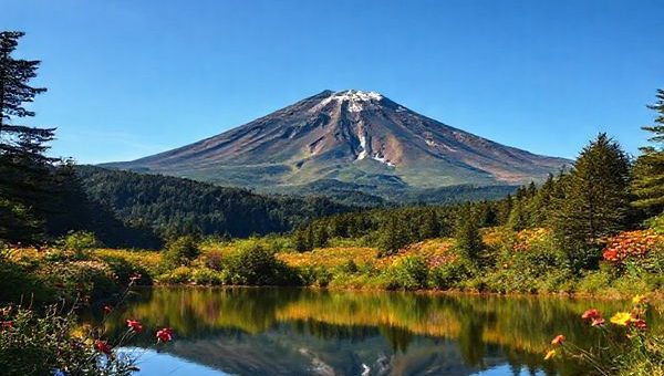 A breathtaking high-definition view of Mount Taranaki, showcasing its iconic symmetrical cone surrounded by lush forests and vibrant wildflowers in full bloom during summer. The scene is alive with native birds flitting through the rich greenery, and a serene reflection of the mountain is visible in the tranquil waters of Lake Mangamahoe below, framed by clear blue skies and warm sunlight. Capture the adventure and beauty of the landscape, inviting viewers to feel the warmth and vibrancy of this hidden gem in New Zealand.
