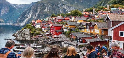 A picturesque Scandinavian landscape featuring a colorful Norwegian town nestled among stunning fjords, with people engaging in language learning—some using apps on their phones, others in conversation with native speakers. Include elements of Norwegian culture like traditional costumes and literature. The scene conveys a vibrant atmosphere of learning and exploration. High definition.