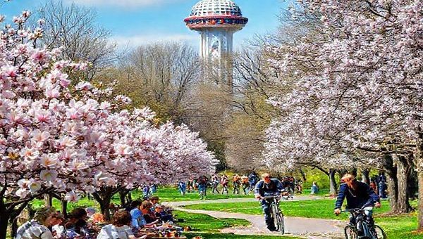 "A vibrant scene of Oberhausen in spring, showcasing cherry blossoms and magnolias in full bloom, with locals enjoying picnics in a park. In the background, the Gasometer stands tall, adorned with colorful decorations. Cyclists are seen along the Emscher Park Bicycle Trail, surrounded by lush landscapes. Capture the energy and beauty of this lively city in high definition."