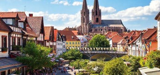A high-definition depiction of Erfurt, Germany, showcasing the vibrant medieval architecture and cobblestone streets. Illustrate the city during summer, with bustling outdoor cafes, lush green parks in full bloom, and colorful festival banners, while capturing the iconic spires of Erfurt Cathedral and the charming Kramer Bridge in the background. Infuse the scene with warm sunlight and joyful tourists enjoying the lively atmosphere.