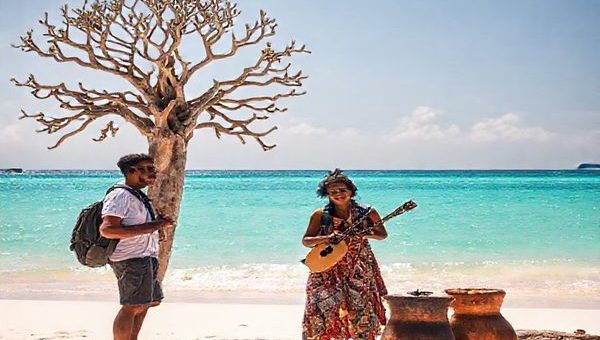 A traveler standing on the stunning beaches of Nosy Be, Madagascar, eagerly practicing Malagasy phrases with a friendly local beside a vibrant baobab tree, with turquoise waters sparkling in the background. Include cultural elements like traditional music instruments and local crafts. High definition.