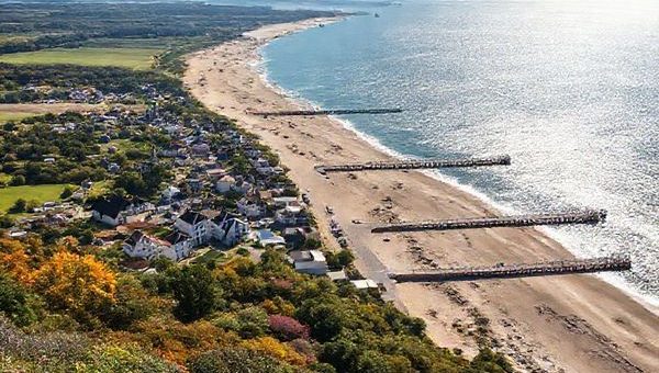 A breathtaking view of Usedom Island showcasing its diverse seasonal beauty: in summer, vibrant beachgoers enjoying sunny shores; in autumn, golden foliage along scenic trails; in winter, serene snow-covered landscapes; and in spring, blooming flowers amid lush greenery. The historic seaside resorts with distinct architecture and long piers should be visible, set against the backdrop of the sparkling Baltic Sea. Capture this charm in high definition.